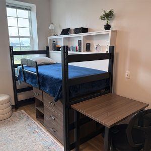UNCW dorm room with Dorm Wise cubby placed behind a lofted bed, holding everyday items like water bottles and tech devices.