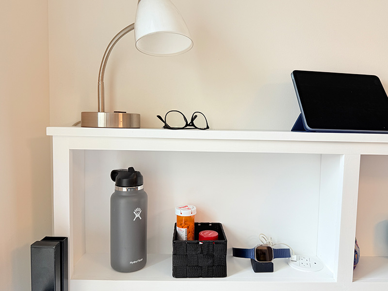 Dorm Wise cubby shelf organized with lamp, glasses, iPad, watch, medicine, and water bottle on and in the shelf.